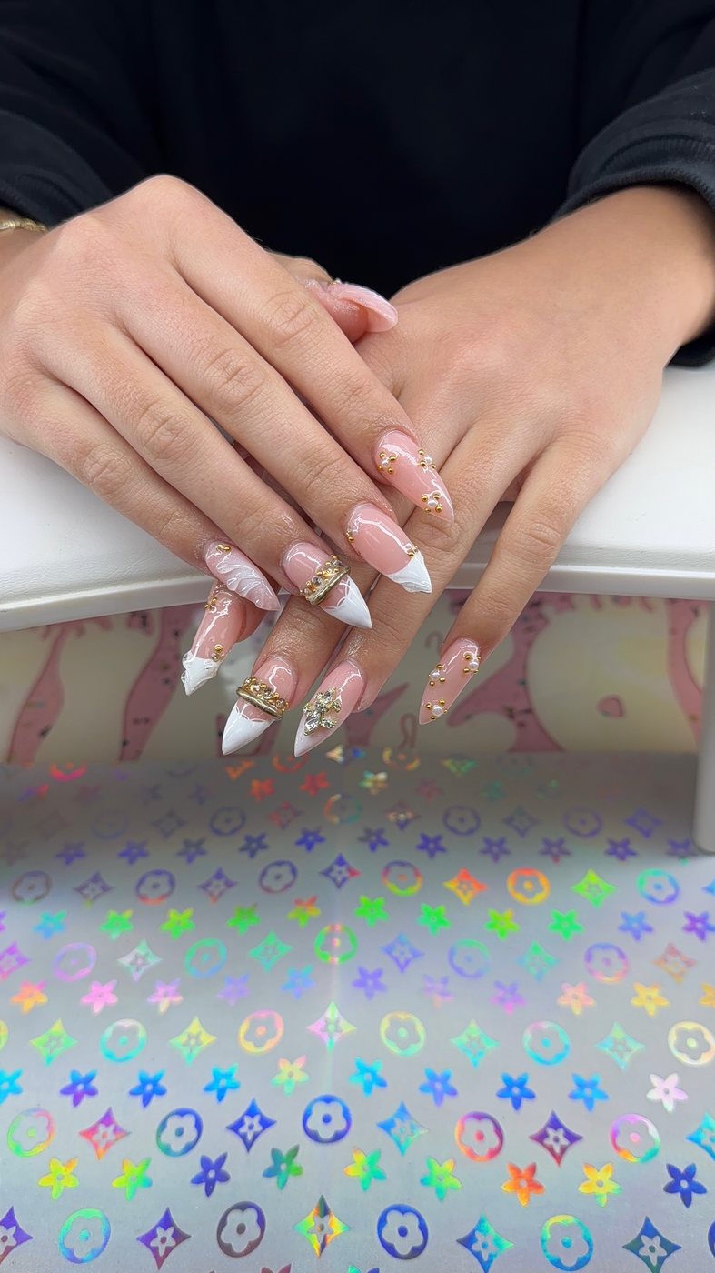 Serenity nail art with white sculpted tips, gold charms, and rhinestone accents.